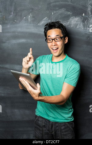 Nachdenklicher asiatischen Mann mit einem Tablet-PC stehen neben einer Tafel. Stockfoto