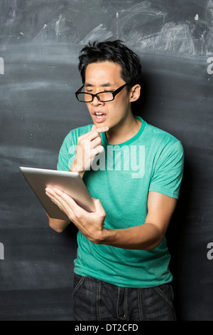 Nachdenklicher asiatischen Mann mit einem Tablet-PC stehen neben einer Tafel. Stockfoto