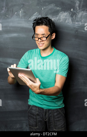 Nachdenklicher asiatischen Mann mit einem Tablet-PC stehen neben einer Tafel. Stockfoto