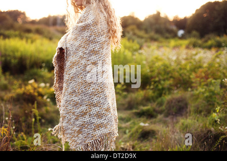Junge Frau bedeckt mit Decke stehend auf Wiese, Mittelteil Stockfoto