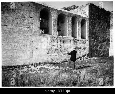 Ein Foto eines Mannes, der die Glocken im Glockenturm der San Juan Capistrano Mission läutet, aufgenommen um 1900, um einen Moment religiöser und kultureller Praxis festzuhalten. Stockfoto