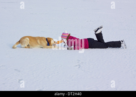 Mädchen mit Schlittschuhen spielen mit ihrem Hund auf zugefrorenen See ziehen die Hundespielzeug mit den Zähnen Stockfoto
