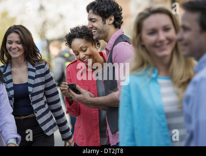 Menschen im Freien in der Stadt im Frühjahr Zeit zwei Blick auf einem Handy-Bildschirm und lachen Stockfoto