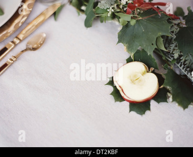 Eine Tischplatte weiße Tuch A Gedeck mit Besteck und Teller einen Apfel halbiert und grünem Laub Tischdekoration Stockfoto
