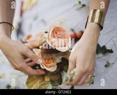 Eine Frau, die Vermittlung von frischen Blumen auf einem Tisch bedeckt mit einem weißen Tuch Pfirsich farbigen Rosen Stockfoto