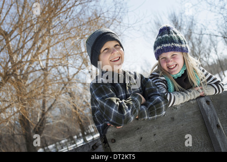 Winterlandschaft mit Schnee auf dem Boden zwei Kinder in Strickmützen stützte sich auf einen Zaun Stockfoto