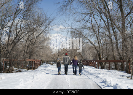 Winterlandschaft mit Schnee auf dem Boden A Familie Erwachsene und zwei Kinder, die eine leere Straße hinunter Stockfoto