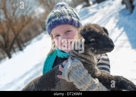 Winterlandschaft mit Schnee auf dem Boden A junges Mädchen hält ein junges Lamm Stockfoto