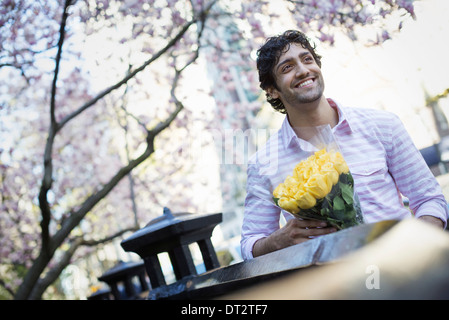 Ein junger Mann in der Park im Frühling hält eine Reihe von gelben Rosen Stockfoto