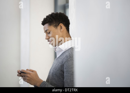 Ein junger Mann in einem grauen Pullover mit seinem Mobiltelefon Stockfoto