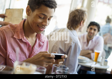 Urban Lifestyle drei junge Männer in einem Café eine Überprüfung seiner Smart Telefon zwei an einem Tisch im Gespräch Stockfoto