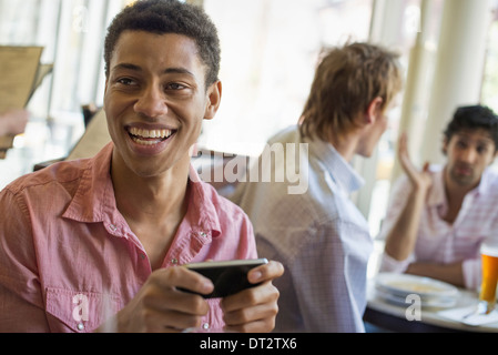 Urban Lifestyle drei junge Männer in einem Café eine Überprüfung seiner Smart Telefon zwei an einem Tisch im Gespräch Stockfoto