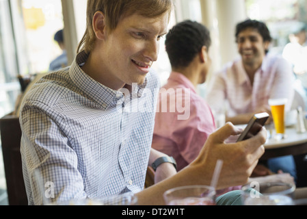 Urban Lifestyle drei junge Männer in einem Café eine Überprüfung seiner Smart Telefon zwei an einem Tisch im Gespräch Stockfoto