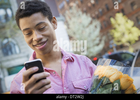 Urban Lifestyle A junger Mann mit kurzen schwarzen Haaren, trägt ein rosa casual Hemd Holding ein smart phone Stockfoto