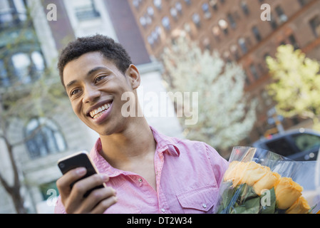 Urban Lifestyle A junger Mann mit kurzen schwarzen Haaren, trägt ein rosa casual Hemd Holding ein smart phone Stockfoto