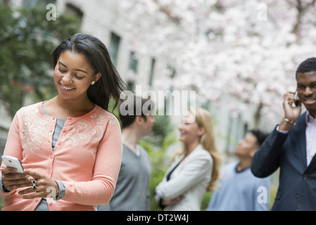 Blick über Citycity Park eine Frau in einem rosa Hemd überprüft ihr Handy vier Personen im Hintergrund Stockfoto