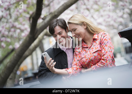 Blick über CityYoung Menschen im Freien parken, eine junge Frau und Mann sitzen nebeneinander blickte auf ein smart phone Stockfoto