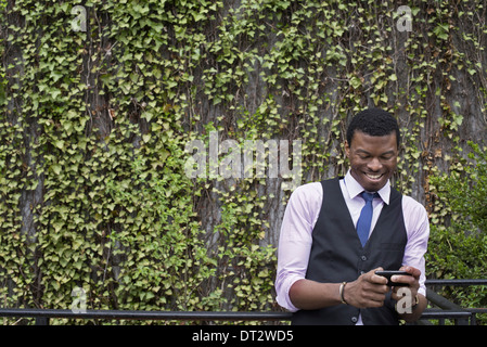Stadtmauer Park bedeckt Kletterpflanzen und Efeu A junger Mann in eine Weste Hemd und Krawatte sein Telefon überprüfen Stockfoto