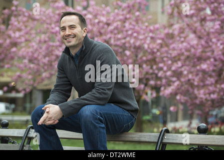 Ein Mann sitzt auf der Rückseite einer Parkbank unter den Kirschblüten im park Stockfoto
