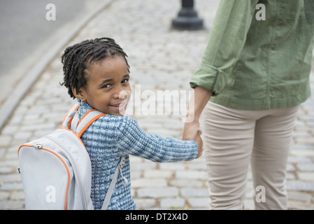 New York City Sonnenschein und Kirschen blühen ein Junge trägt eine Schule Schultasche und hand in hand gehen mit einer Frau Stockfoto