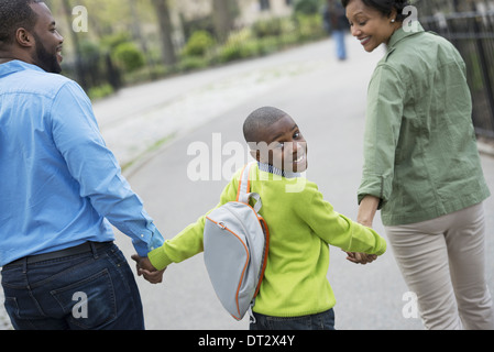 Ein Junge mit einer Schultasche, Hand in Hand mit seiner Mutter und Vater Stockfoto