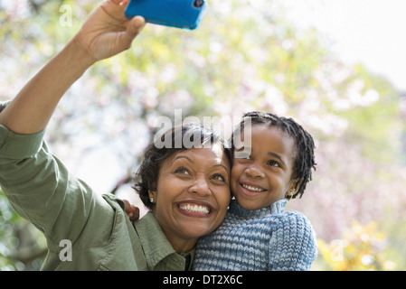 Sonnenschein und Kirschblüte A Mutter und Sohn posieren für ein Foto mit einem Smartphone Stockfoto