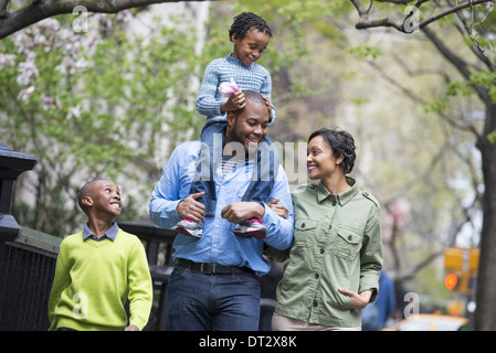 Eine Familie Eltern und zwei jungen A Child auf seines Vaters Schultern Reiten Stockfoto