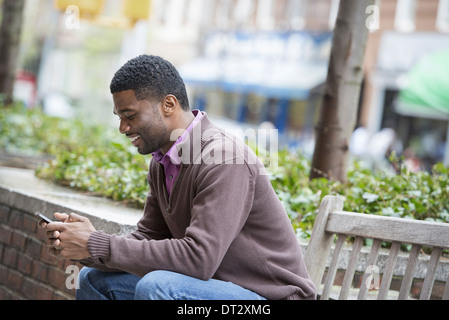 Ein junger Mann sitzt auf einer Bank überprüft seine Telefon und SMS Stockfoto