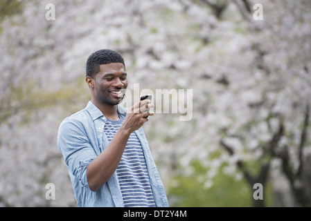 Ein Mann steht unter einem Baum mit Blüte Blick auf sein Handy laden Stockfoto