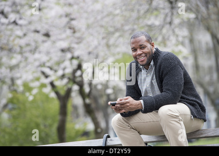 Ein Mann sitzt auf einer Bank im Park hält eine Telefon Stockfoto