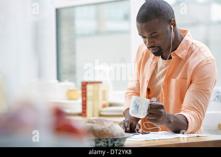 Ein Mann in einem orangefarbenen t-Shirt beim Frühstück mit einer Tasse Tee Stockfoto