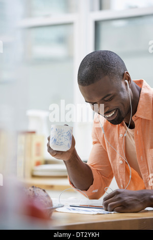 Ein Mann in einem orangefarbenen t-Shirt beim Frühstück mit einer Tasse Tee Stockfoto