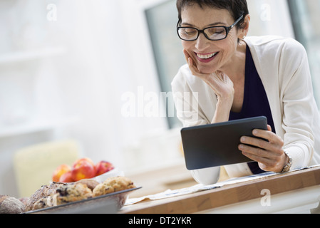 New York City eine Frau gekleidet für die Arbeit in Creme Jacke hält eine Tasse Kaffee, die Überprüfung ihrer digital-Tablette Stockfoto