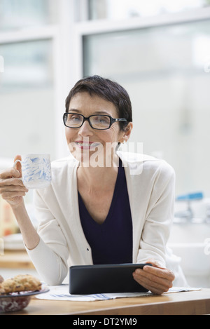 New York City eine Frau gekleidet für die Arbeit in Creme Jacke hält eine Tasse Kaffee, die Überprüfung ihrer digital-Tablette Stockfoto