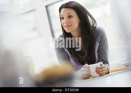 Ein Büro oder eine Wohnung in New York City A junge Frau mit langen schwarzen Haaren, einer Tasse Kaffee innen Stockfoto