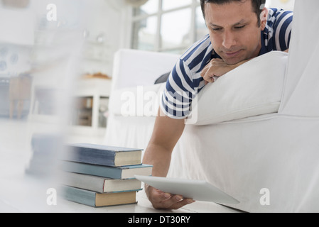 Mann liegt auf seiner Vorderseite auf einem Sofa in einer ruhigen luftig Büroumgebung mit einem digitalen tablet Stockfoto