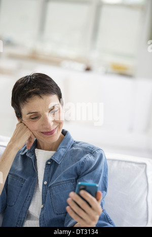 Eine reife Frau mit grauen Haaren tragen ein Jeanshemd Blick auf dem Bildschirm eines smart phone Stockfoto