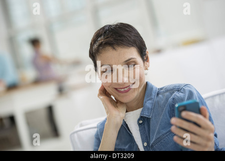 Profis im Büro A Licht und luftig Ort der Arbeit eine reife Frau in ein blaues Jeanshemd, das Betrachten eines blauen smart phone Stockfoto