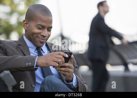 Ein Mann sitzt mit seinen intelligenten Telefon A Mann im Hintergrund Stockfoto