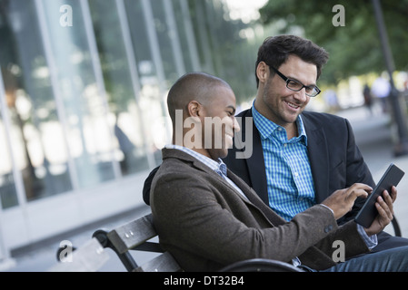 Zwei Männer sitzen auf einer Parkbank im Freien mit Blick auf eine digital-Tablette Stockfoto