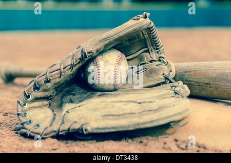 Traditionelle Baseball mit Ball im Handschuh und Fledermaus auf Basis auf Feld. Feldspieler Wand im Hintergrund. Stockfoto