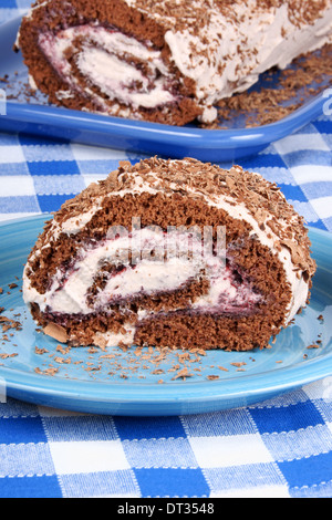 Schokoladen-Biskuitrolle Kuchen mit Beeren Marmelade und Sahne über einem karierten Hintergrund. Tiefenschärfe, flachen DOF. Stockfoto