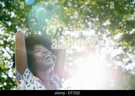 Eine junge Frau in einem geblümten Sommerkleid mit ihren Händen hinter ihrem Kopf lächelnd und blickte Stockfoto