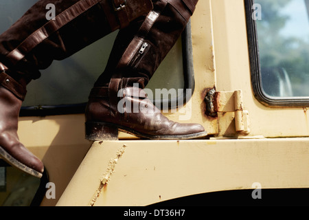 Eine junge Frau in Jeansjacke und Stiefel auf der Motorhaube eines Traktors Stockfoto