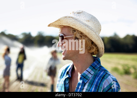 Ein junger Mann in Stroh Hut und eine Sonnenbrille Bewässerung Sprinkler im Feld Stockfoto