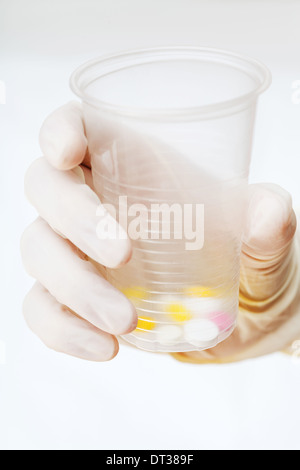 behandschuhten Hand hält Plastikbecher mit Tabletten auf weißem Hintergrund Stockfoto