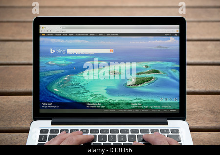 Die Bing-Website auf einem MacBook Hintergrund eine Holzbank im Freien einschließlich eines Mannes Finger (nur zur redaktionellen Verwendung). Stockfoto