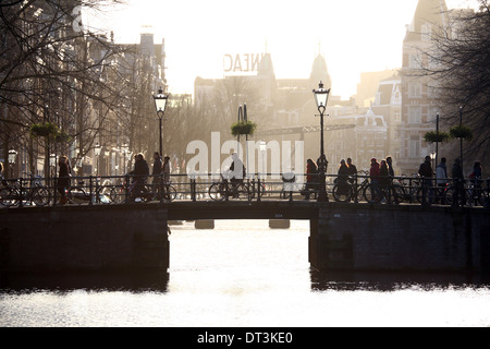 Silhouette von Personen und Fahrrädern fahren über eine Brücke über einen Kanal in Amsterdam, Holland Stockfoto