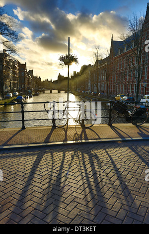 Silhouette von einem abgestellten Fahrrad und seinen Schatten auf einer Brücke über einen Kanal bei Sonnenuntergang in Amsterdam, Holland Stockfoto