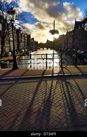 Silhouette von einem abgestellten Fahrrad und seinen Schatten auf einer Brücke über einen Kanal bei Sonnenuntergang in Amsterdam, Holland Stockfoto